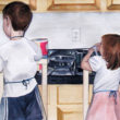 Watercolor painting of two children helping cook in the kitchen.
